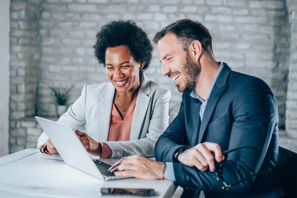 Two smiling diverse professionals working together on a laptop.