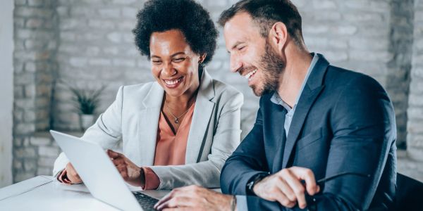 Two colleagues smiling while looking at a laptop.