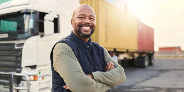 Smiling truck driver standing confidently in front of his truck.