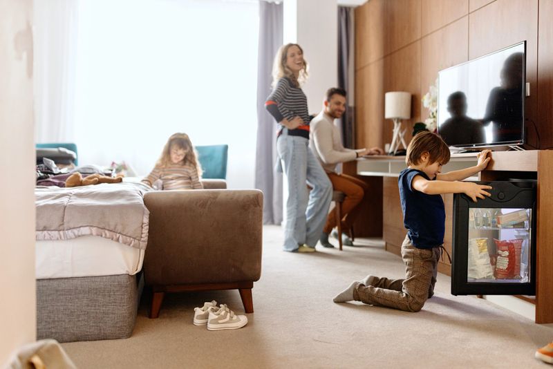 Family unpacking/ packing in hotel room, father is working on laptop, kids are watching cartoons