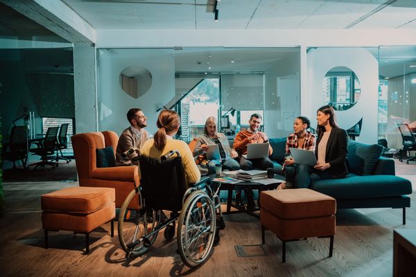 Diverse team collaborating in a modern office lounge, including a person in a wheelchair.