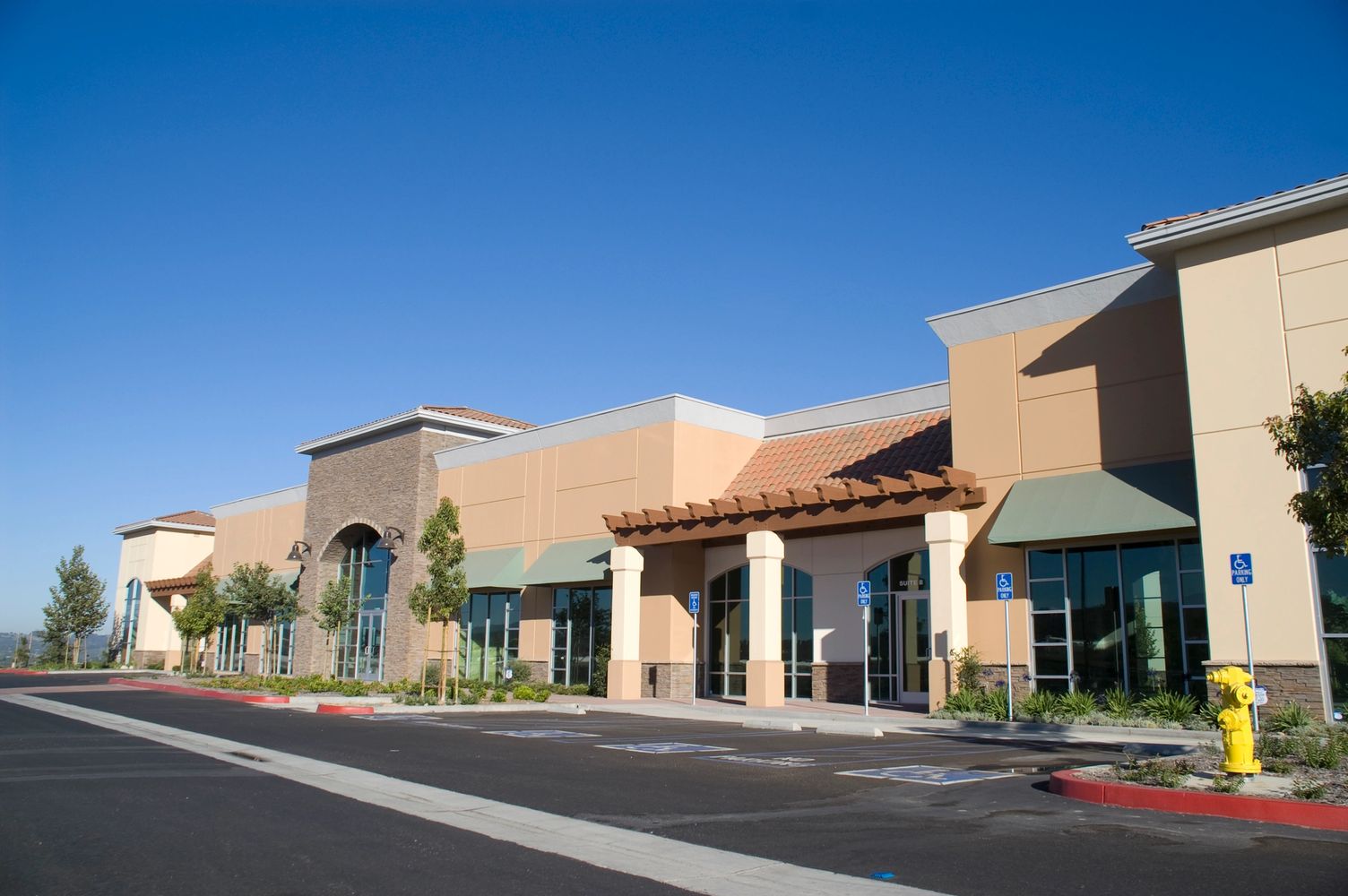 Empty commercial building with handicap parking spaces under clear blue sky.