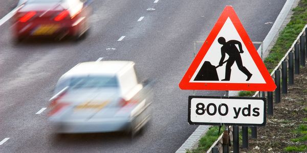 Roadwork warning sign on a highway with blurred cars passing by.