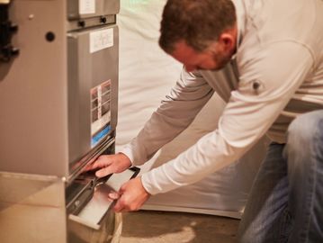 Technician inspecting and repairing a furnace in a basement.