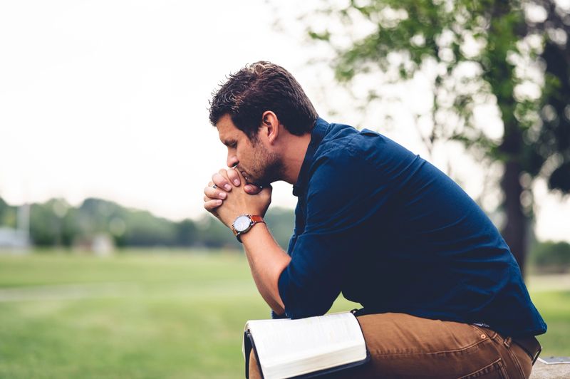 A shallow focus of a male Caucasian praying earnestly at a park in grayscale