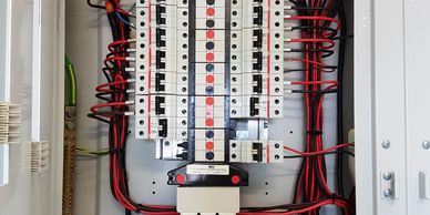 Organized electrical panel with circuit breakers and neatly arranged red and black wires.