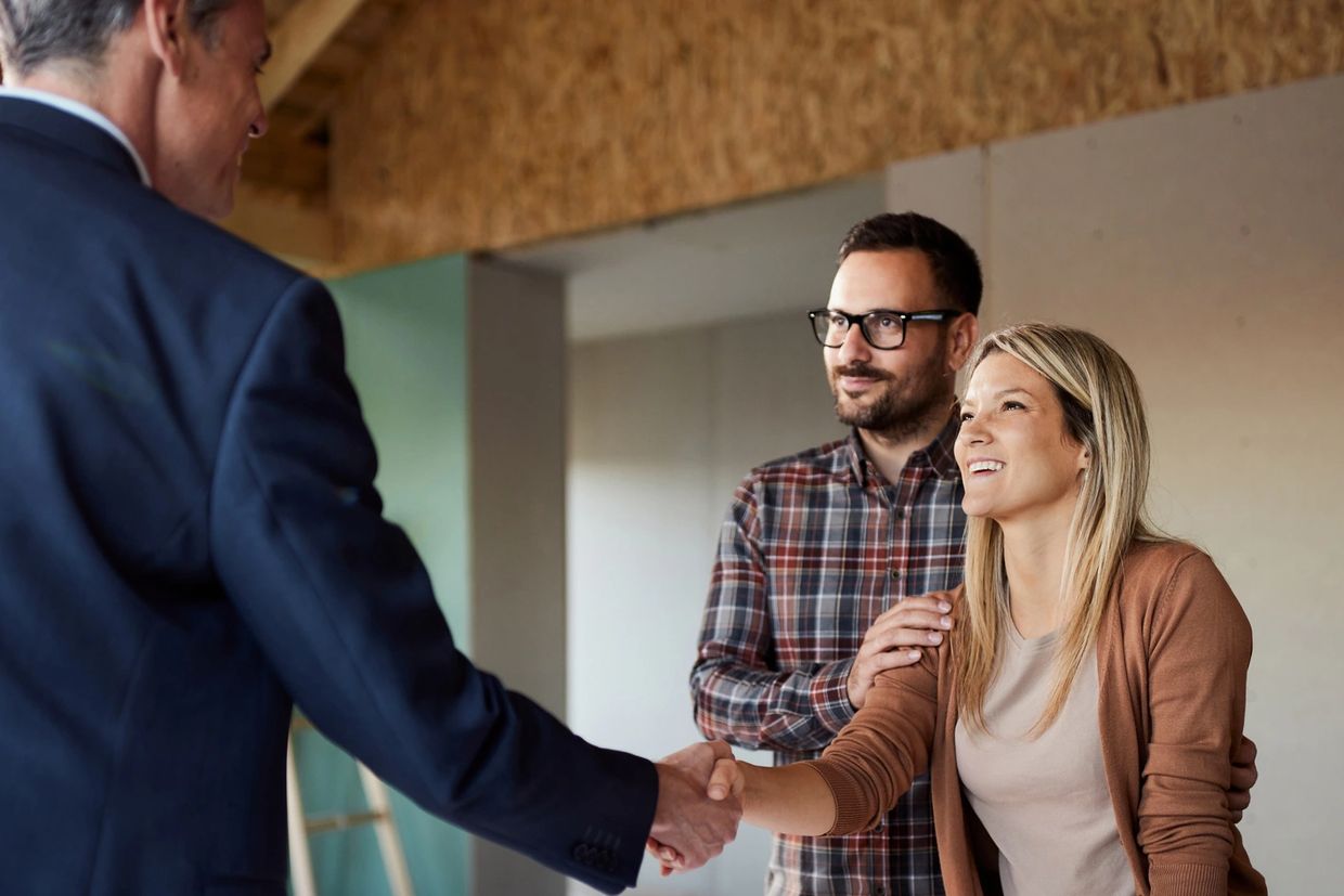 Couple shaking hands with a professional over building plans indoors.