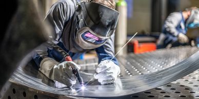 A welder in protective gear welding a large metal sheet.