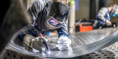 Worker welding metal with protective gear in industrial setting.