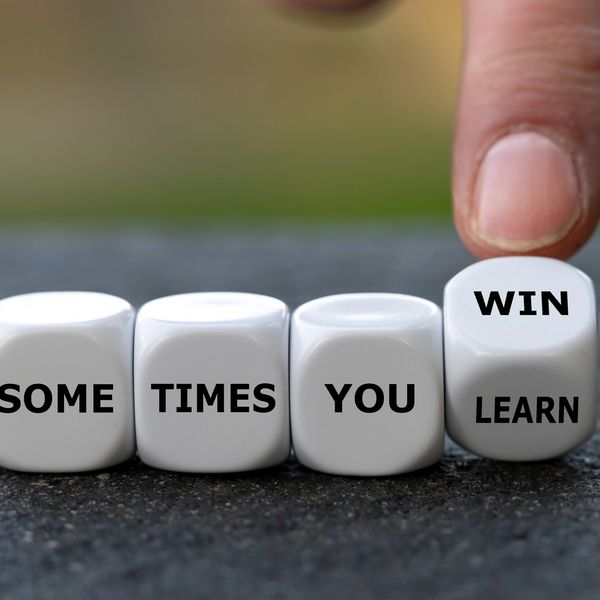 Dice spelling out 'Sometimes you win, sometimes you learn' with a finger turning the last die.