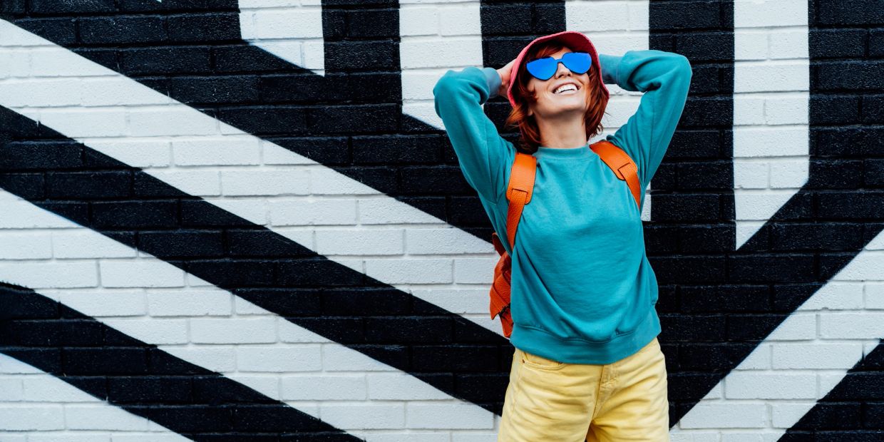 Smiling woman in colorful outfit posing against black and white graffiti wall.
