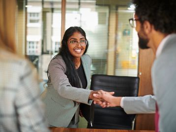 Woman smiling while shaking hands at office.