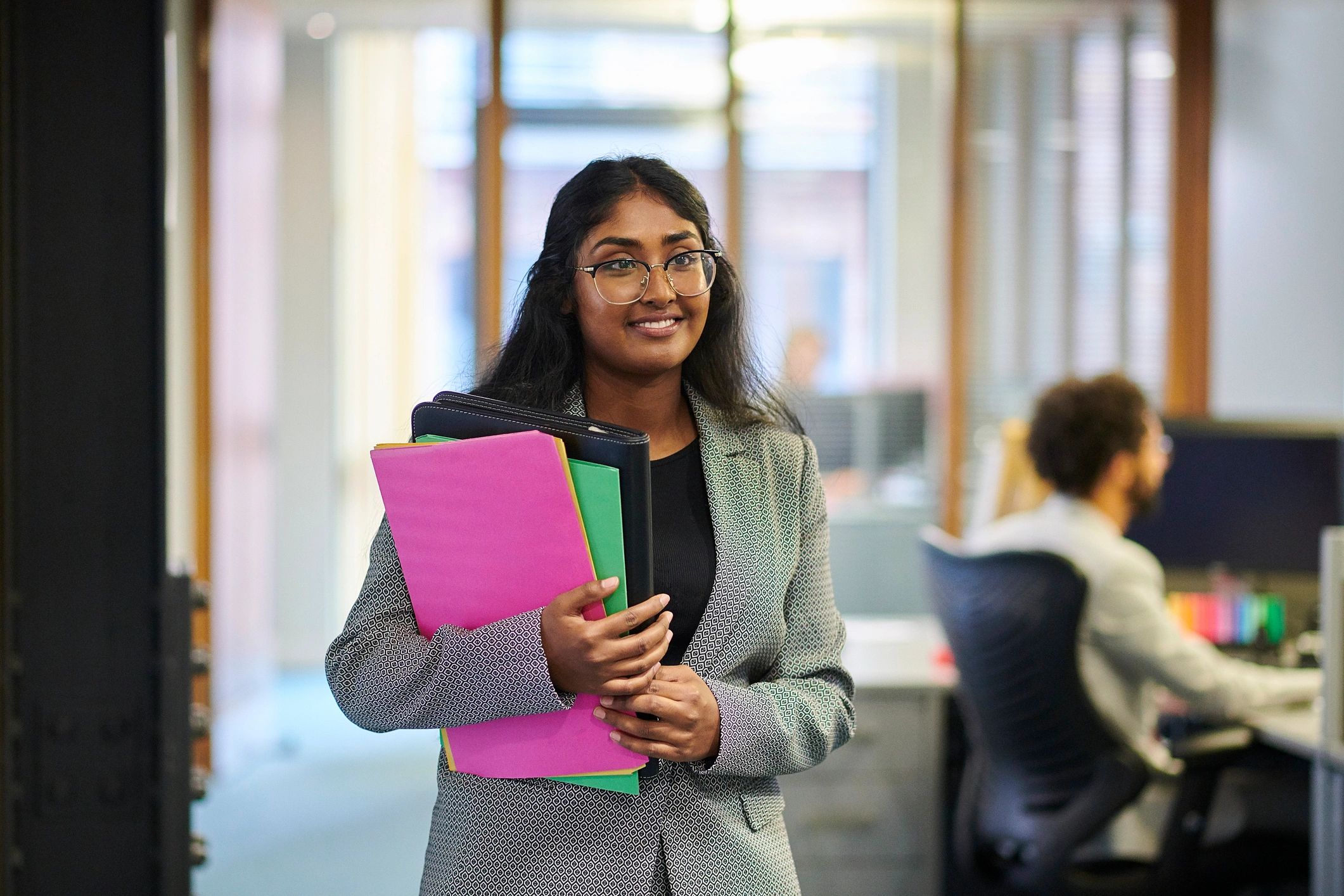 Smiling woman holding colorful folders in an office.