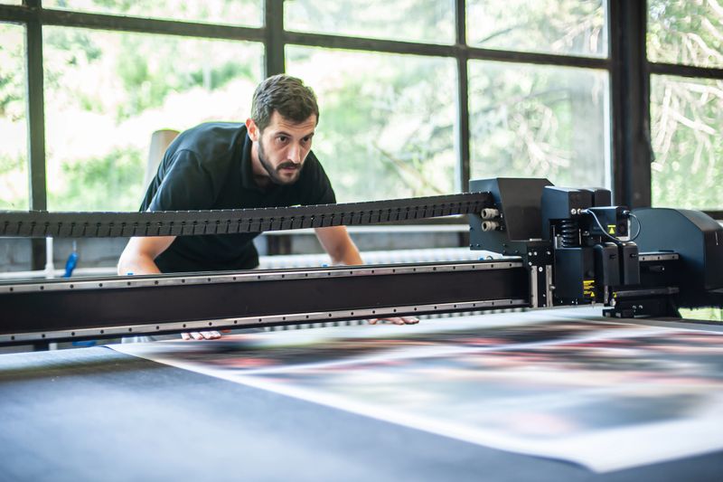 Professional worker printmaker technician operator works in printing press hall and printshop office with many different type of machine