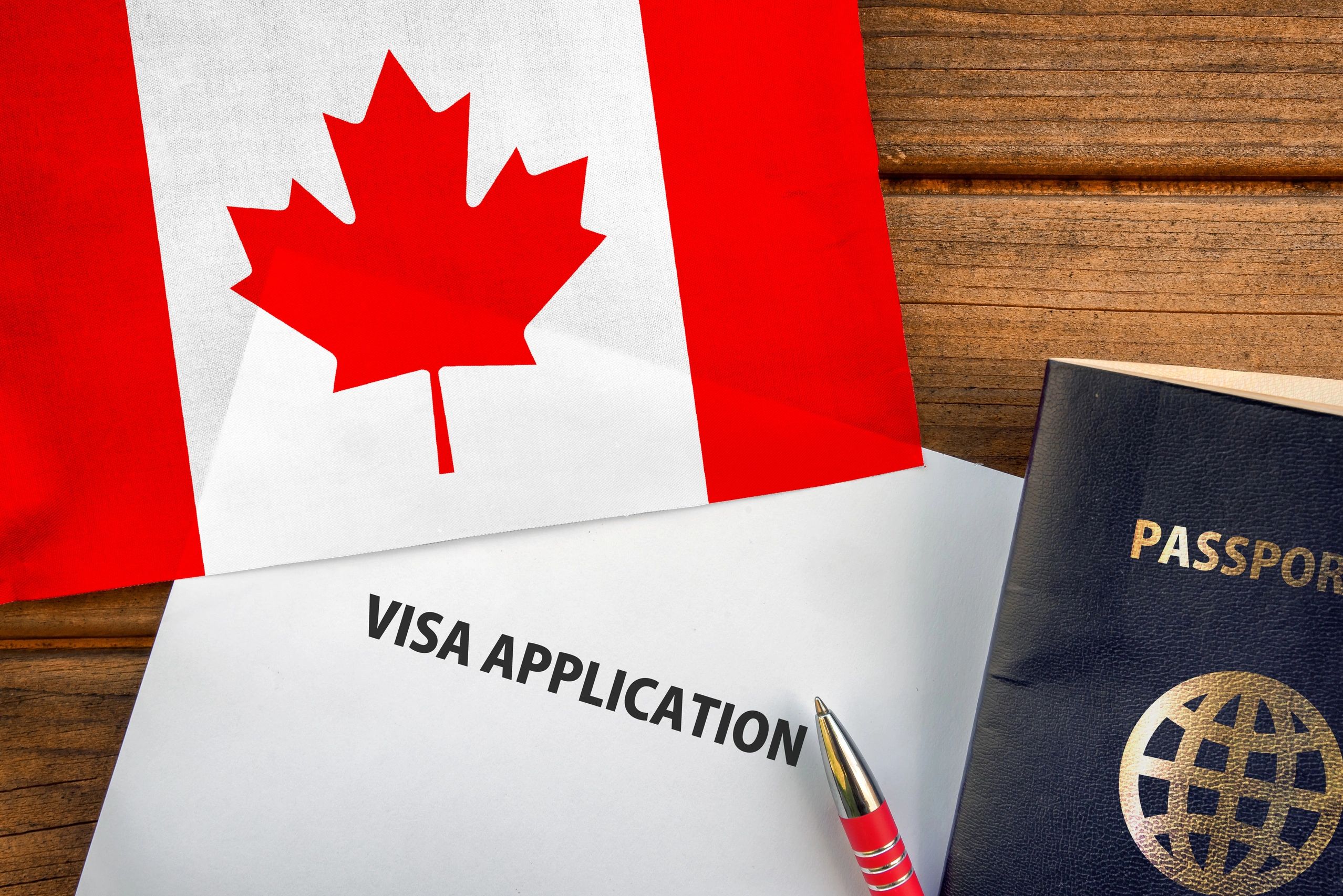 Canadian visa application with passport and pen on wooden table.