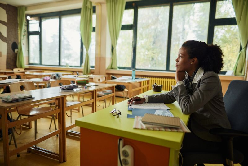 African American female teacher brainstorming while working on exam papers at elementary school.