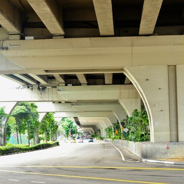City road running beneath a concrete overpass with greenery on the sides.