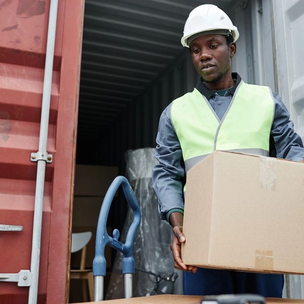 Worker in safety gear handling a cardboard box near a shipping container.