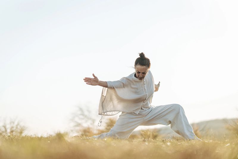 Woman practicing tai chi chuan on a meadow in nature alone. Chinese management skill Qi's energy.