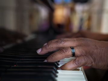 Close-up of a hand with a ring playing piano keys.