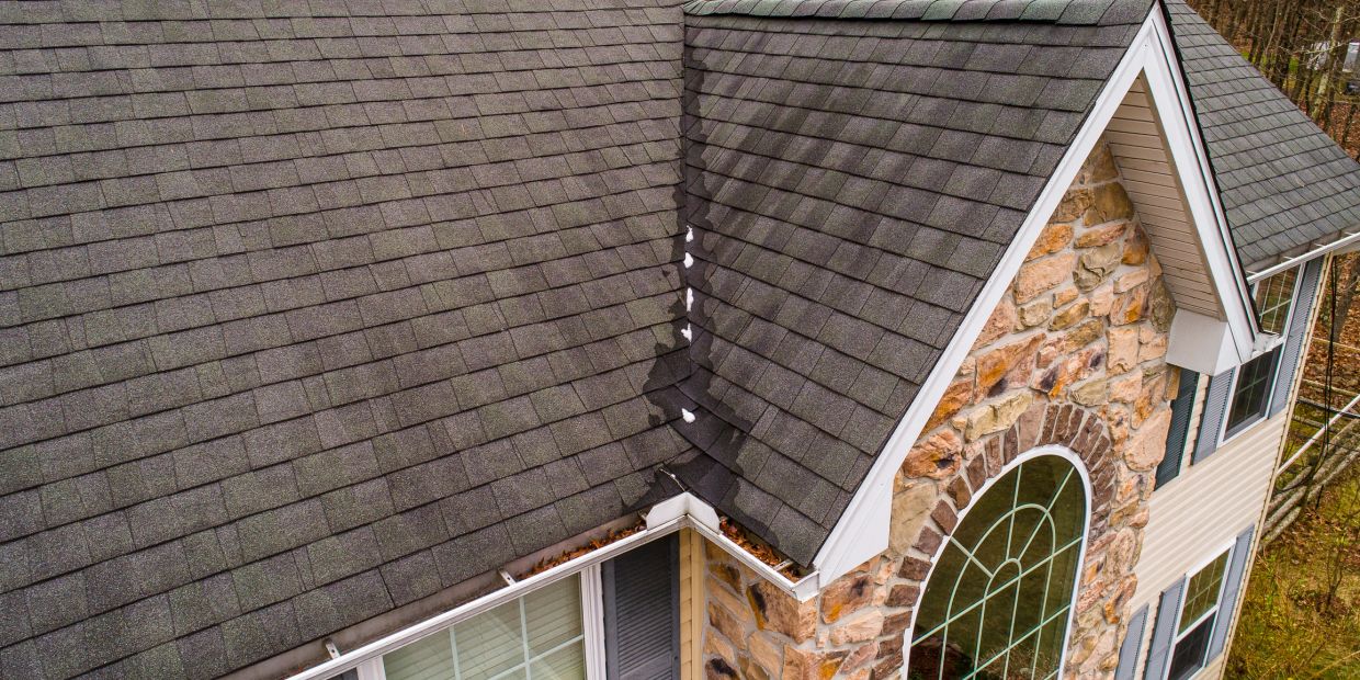 Close-up of a house roof with a stone wall and windows.