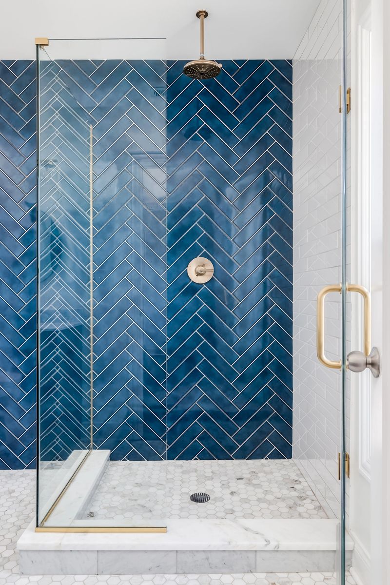 A blue single herringbone tiled shower in a luxury home with gold hardware.