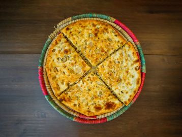 Four slices of golden flatbread with sesame seeds on a round colorful woven tray.