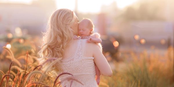 Mother holding baby in a sunlit field.