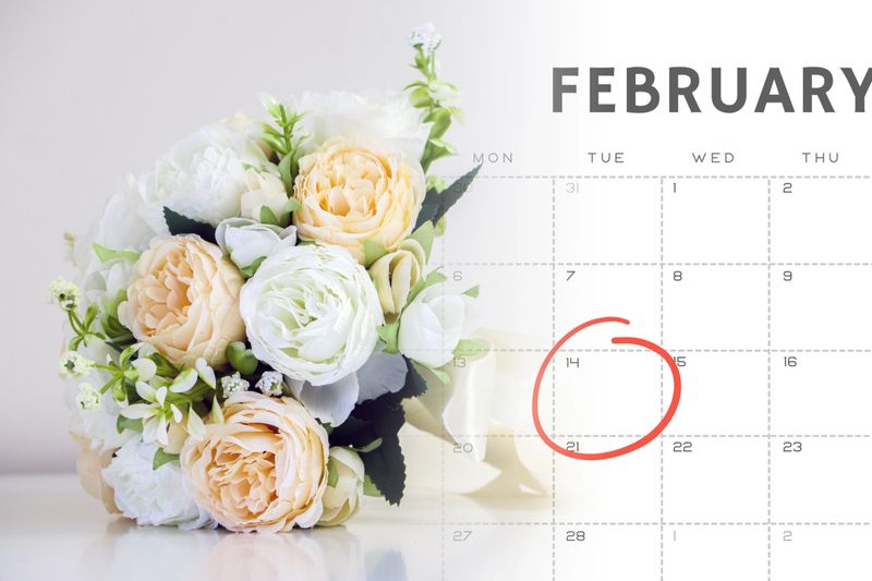 Pretty bouquet of wedding flowers, white and peach roses, over February calendar with 14th Valentines day marked with a red circle, Valentines, love, romance and wedding concept