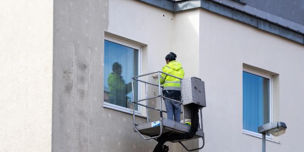 Worker in yellow jacket cleaning window from elevated platform.
