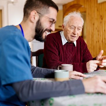 A young caregiver and elderly man sharing a moment at the table with coffee.