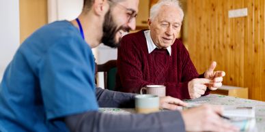 A caregiver and elderly man engaged in a joyful conversation at a table.