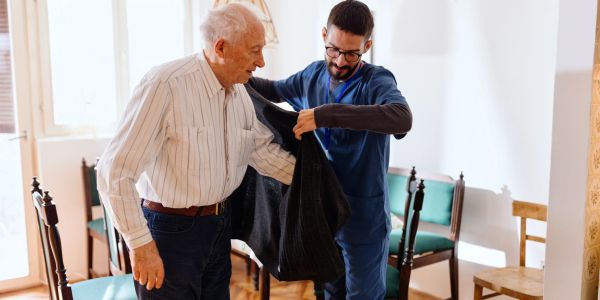 A man helps an elderly man put on a jacket.