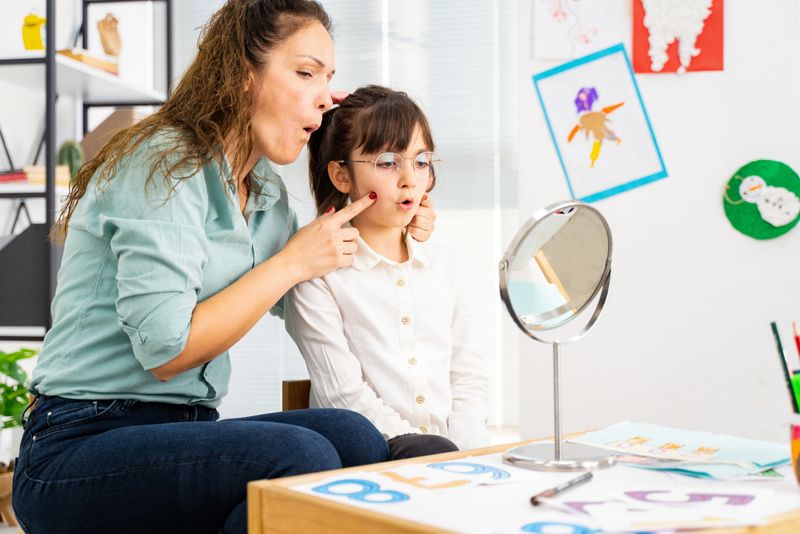 girl in speech therapy office. Mirror reflection of young girl exercising correct pronunciation with speech therapist
