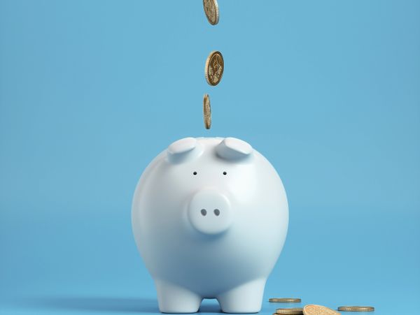 White piggy bank with coins dropping in, on a blue background.