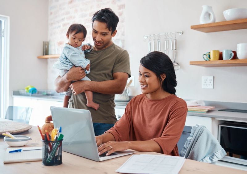Internet, family and parents doing research on down syndrome with baby on a laptop in their house. Mother and father with smile for child and working on taxes or finance budget on the computer