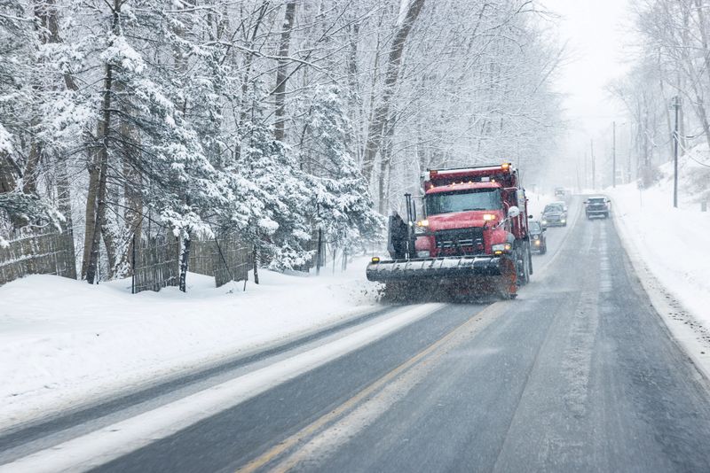 Snow plow truck clearing snow from a road during a winter storm