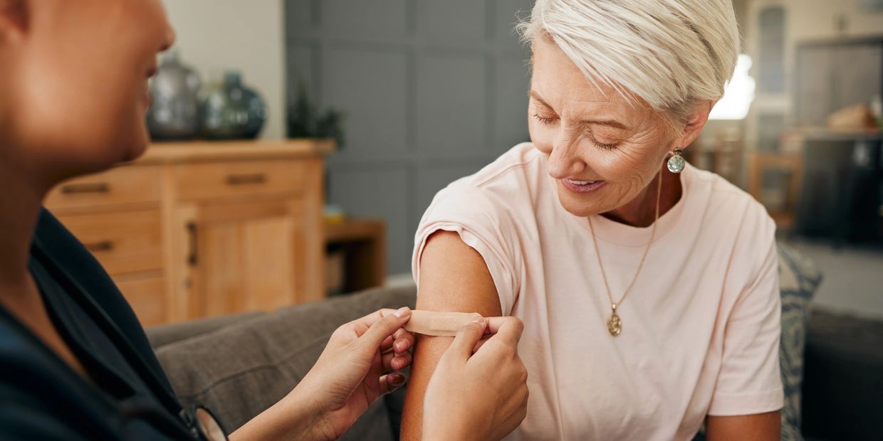 Caregiver applying a bandage to a senior client's arm during in-home wound care