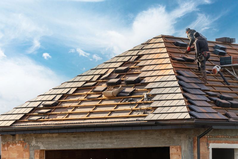 process of building, roofer workers installing grey metal tile on top of roof with wooden frame outdoors on blue sky background
