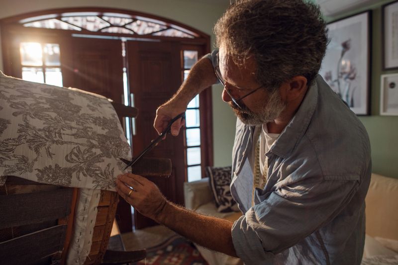 An experienced upholsterer staples the material to a new armchair.