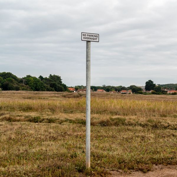A solitary signpost in a field reads 'No Parking Overnight.'