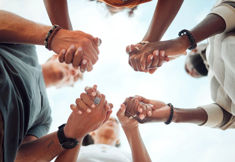 A group of diverse people engaging in a prayer circle outdoors.