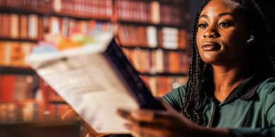 Woman reading a book in a library with focused expression.
