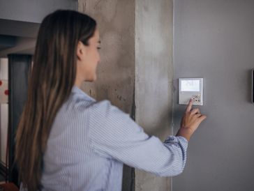 Woman interacting with a smart thermostat on the wall.