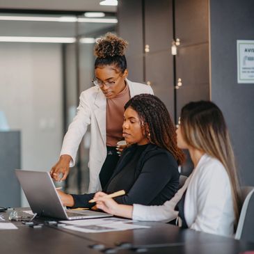 Three women collaborating around a laptop in an office.