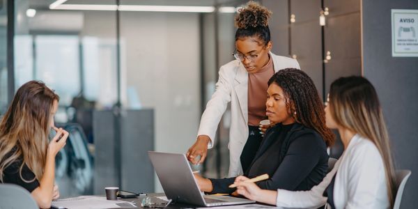 Four women collaborating in a modern office around a laptop and documents.