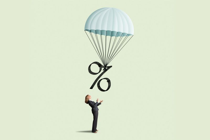 A woman looks up as an interest rate symbol is being slowly lowered via a parachute illustrating the concept of an economic soft landing.