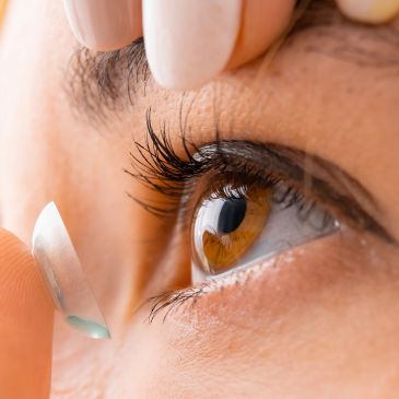 Inserting a contact lens into a brown eye.