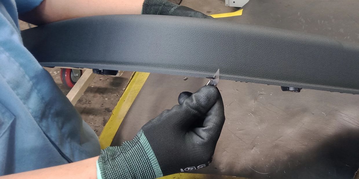 Person wearing gloves holding a sharp blade near a car interior part.