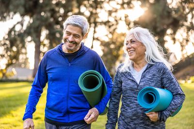 Happy senior couple holding yoga mats and walking outdoors.